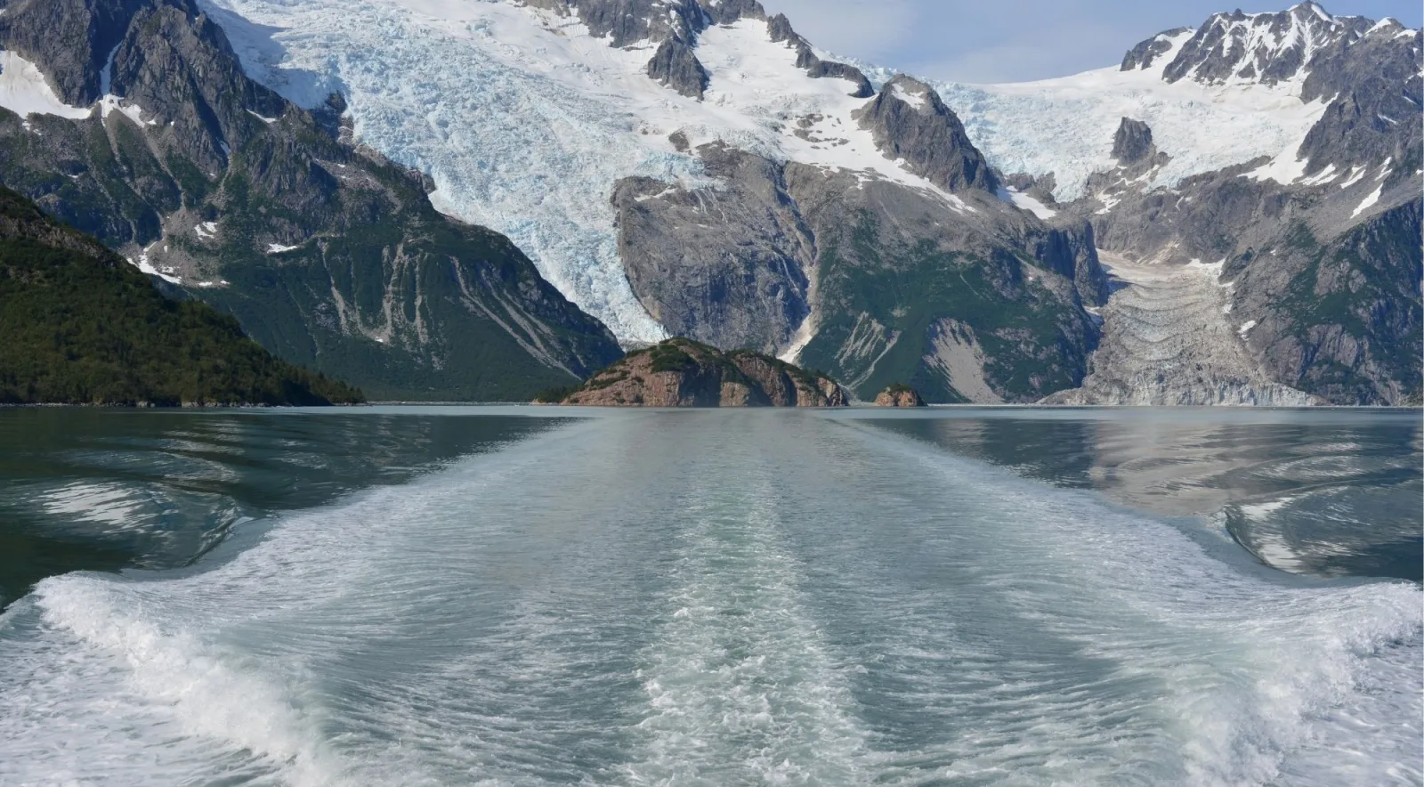 The wake of a tour boat leading back toward hanging glaciers on the fjord walls