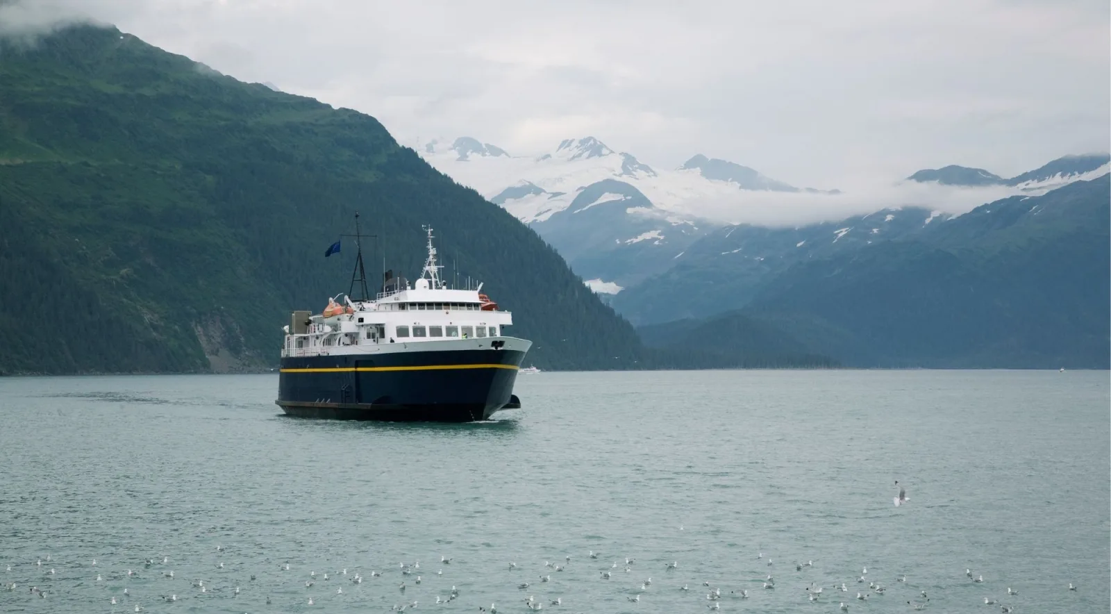 A small tour boat crossing a Prince William Sound fjord with glaciers on the far ridge